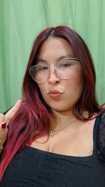 A woman with red hair and glasses on a green background