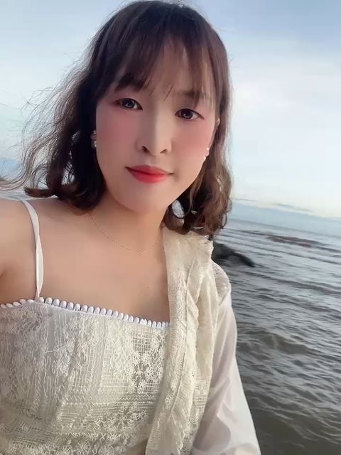A woman in a lace top smiling at her camera by the sea